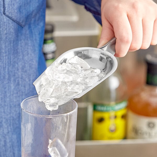 A person using a Choice stainless steel bar scoop to pour ice into a glass.