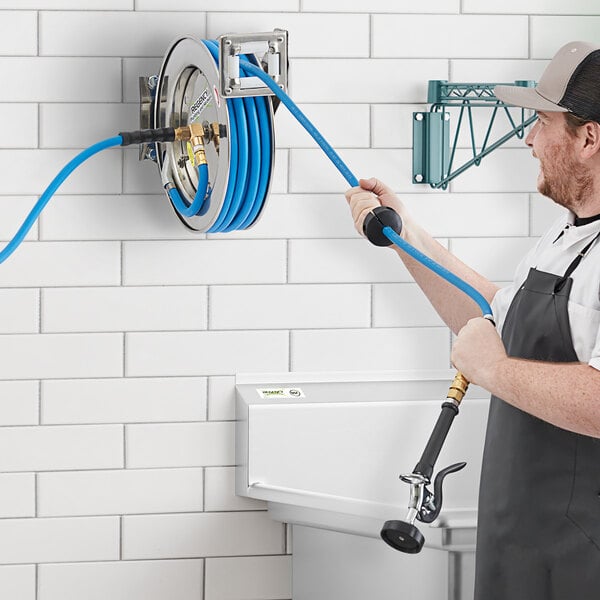 A man in an apron using a Regency stainless steel hose reel with hose and spray valve.