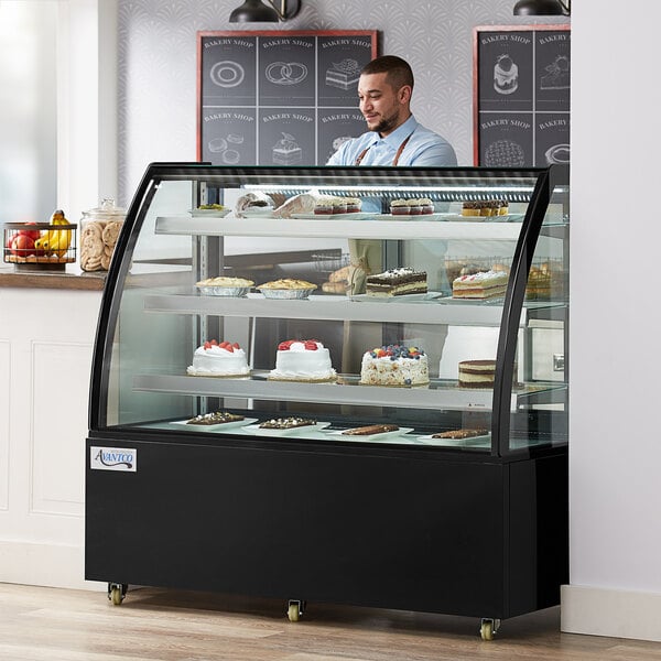 An Avantco refrigerated bakery display case with cakes on shelves and a man in a blue shirt behind it.