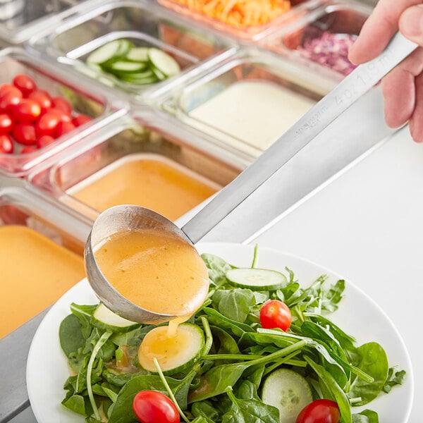 A person using a Choice stainless steel ladle to pour sauce over a bowl of salad.