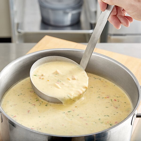 A person using a Choice stainless steel ladle to stir soup in a pot.