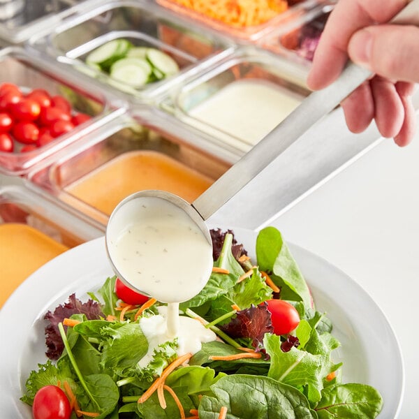 A person using a Choice two-piece stainless steel ladle to pour dressing over a salad.