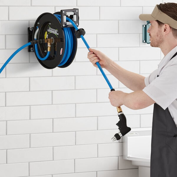 A man holding a Regency hose reel with a hose spraying water.