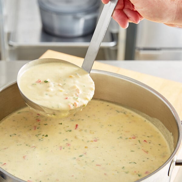 A person holding a Choice stainless steel ladle over a pot of soup.