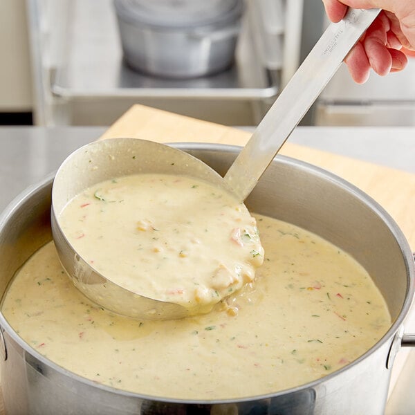 A person using a Choice stainless steel ladle to stir soup in a pot.