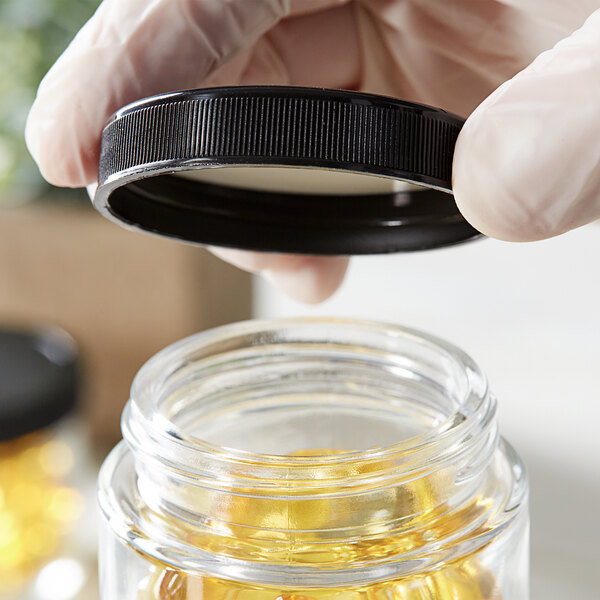 A hand in gloves holding a 53/400 black plastic cap over a jar.