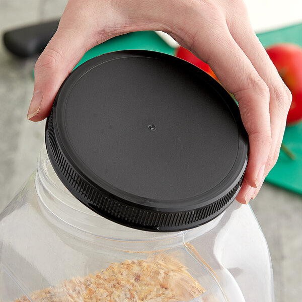 A hand holding a plastic container with a 110/400 unlined black ribbed plastic cap on it.