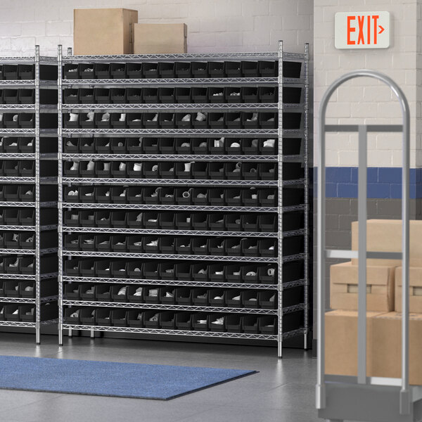 A Regency wire shelving unit with black bins in a storage room filled with boxes.