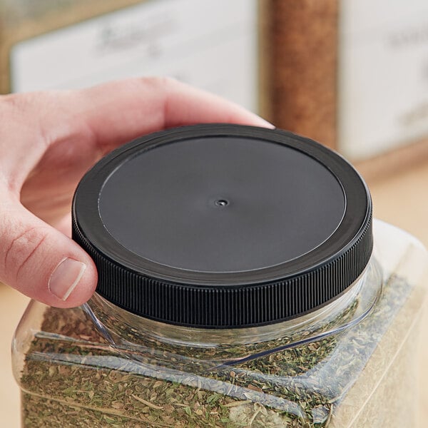 A hand holding a plastic container with a black 89/400 unlined ribbed plastic cap.