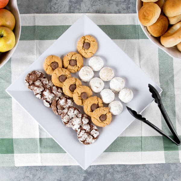 A white square melamine plate with cookies and apples on a table.