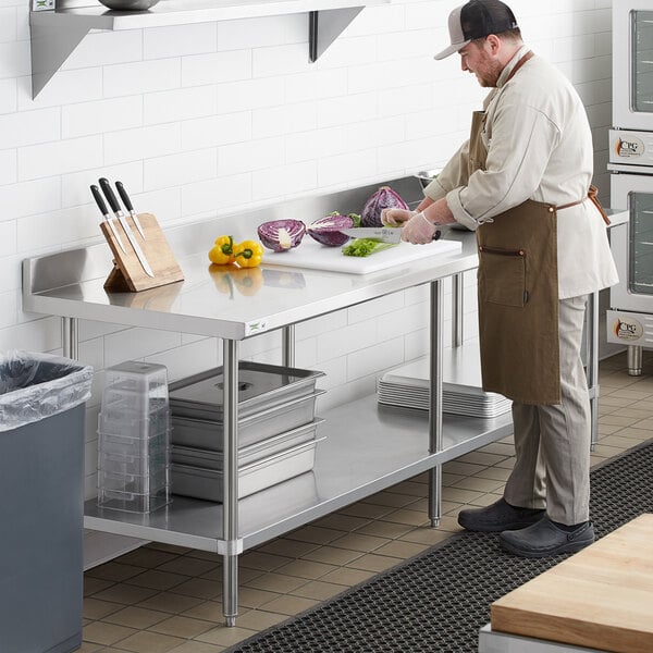 A man in a chef's hat cutting vegetables on a Regency stainless steel work table.