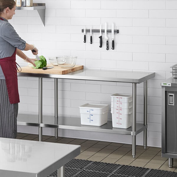 A woman in a red apron cutting vegetables on a Regency stainless steel work table with a metal grate undershelf.