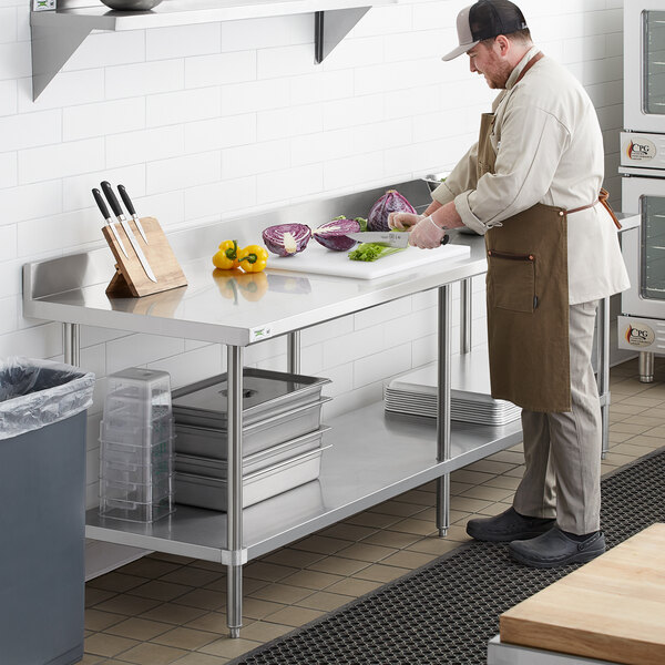 A man in a kitchen cutting vegetables on a Regency stainless steel work table.