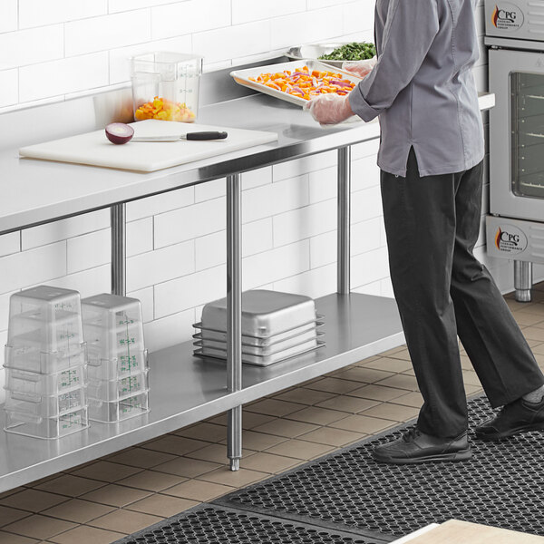 A man standing in front of a Regency stainless steel work table in a kitchen.