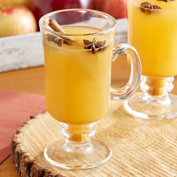 Two glasses of Musselman's apple cider with cinnamon sticks and anise on a table.