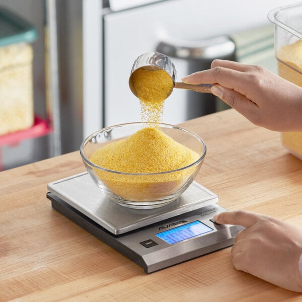 A digital kitchen scale with a glass bowl being filled with yellow granules.