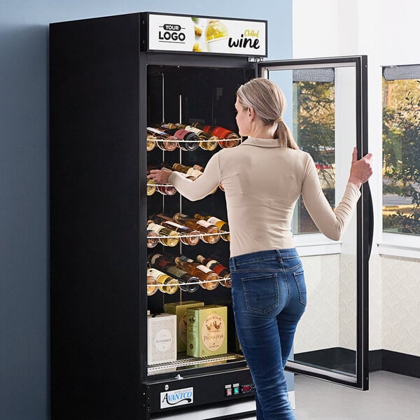 A woman opening the black glass door of an Avantco wine merchandiser.