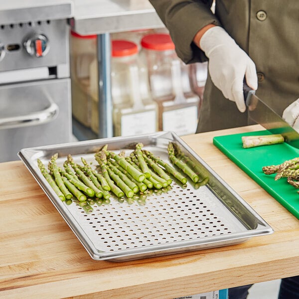 A person cutting asparagus on a Vollrath stainless steel steam table pan.