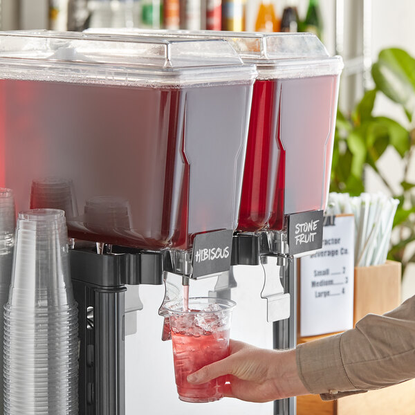 A person pouring Tractor Beverage Co. Organic Hibiscus drink into a beverage dispenser.