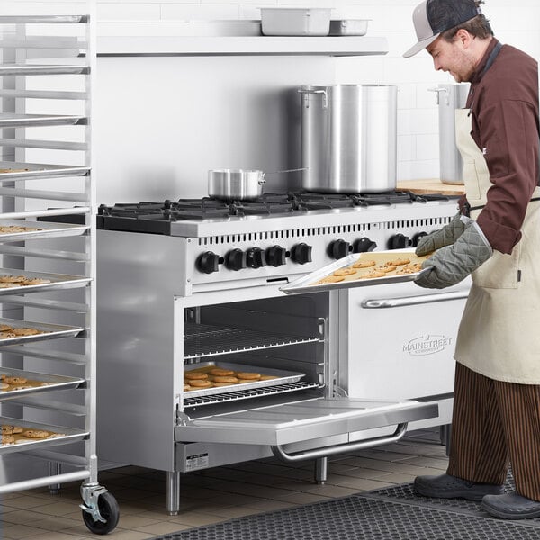 A man in an apron putting cookies in a Main Street Equipment natural gas oven.