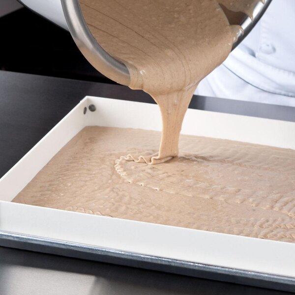 A person pouring brown liquid from a bowl into a white tray using a MFG Tray fiberglass sheet pan extender.
