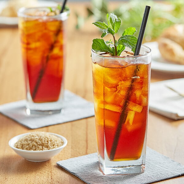 A glass of Tractor Beverage Co. Organic Sweet Tea with a straw and a mint leaf on a table.