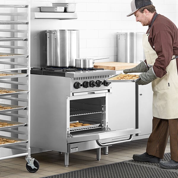 A man wearing a chef's outfit putting cookies into a Main Street Equipment natural gas range.