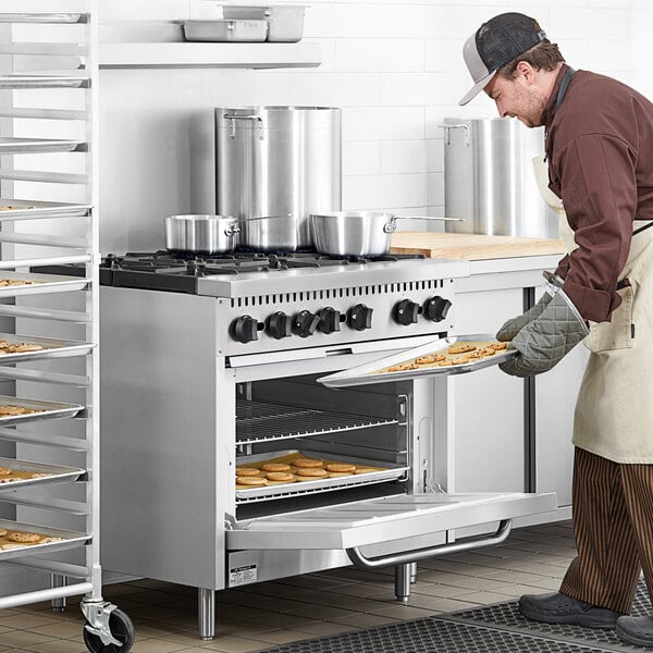 A man wearing a chef's hat using a Main Street Equipment Liquid Propane Range to bake cookies.