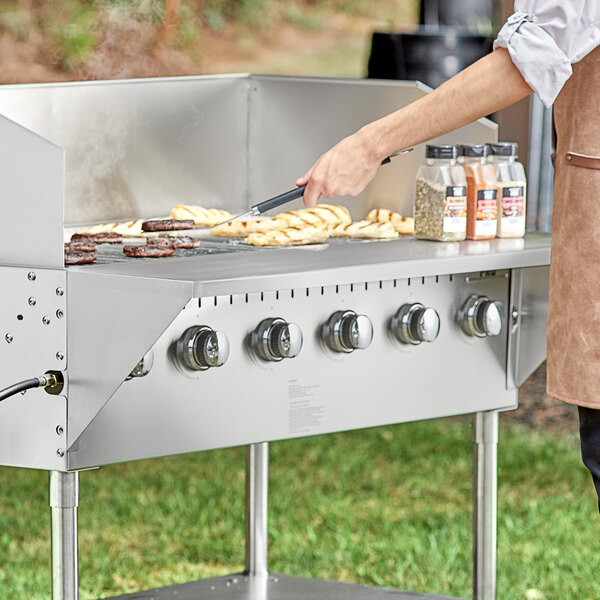 A person cooking food on a stainless steel counter attached to a grill.