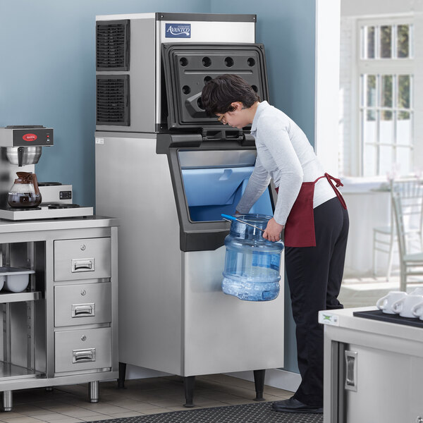 A man putting a container of ice into an Avantco Air Cooled Ice Machine.