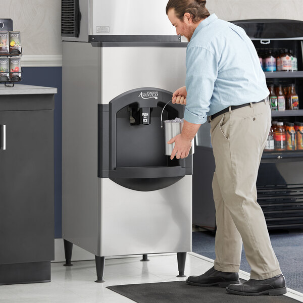 A man holding a bucket of ice next to an Avantco ice machine.