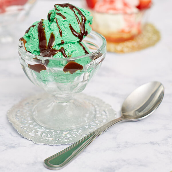 A Libbey glass bowl filled with green ice cream topped with chocolate syrup and a spoon.