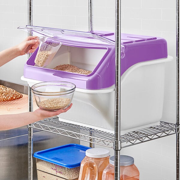 A woman using a Baker's Mark allergen-free ingredient bin with a white lid to pour food into.