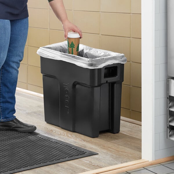 A person putting a cup into a black Toter Slimline trash can.