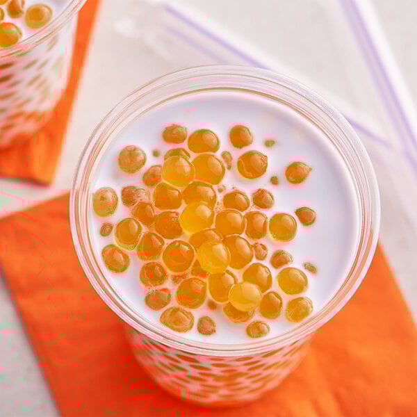 A glass of milk with Fanale Mango Popping Boba floating in it.