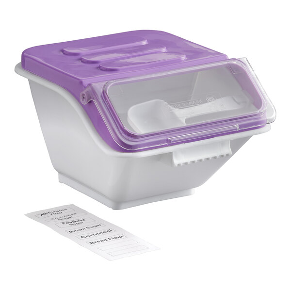 A white ingredient bin with a purple flip lid, a clear front panel, a scoop inside, and a label sheet placed beside it.