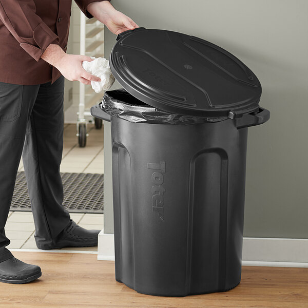 A person cleaning a Toter black trash can with a white cloth.