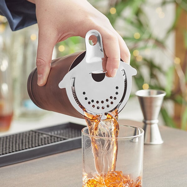 A person using a Franmara stainless steel cocktail strainer to pour a drink into a glass.