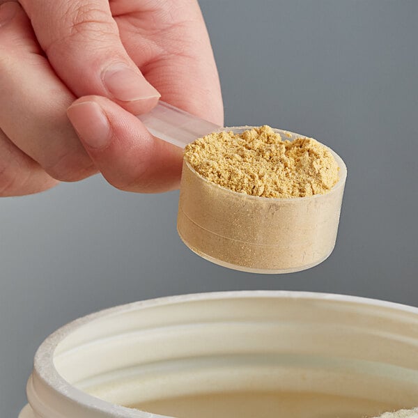 A hand using a Polypropylene scoop to measure yellow powder into a container.