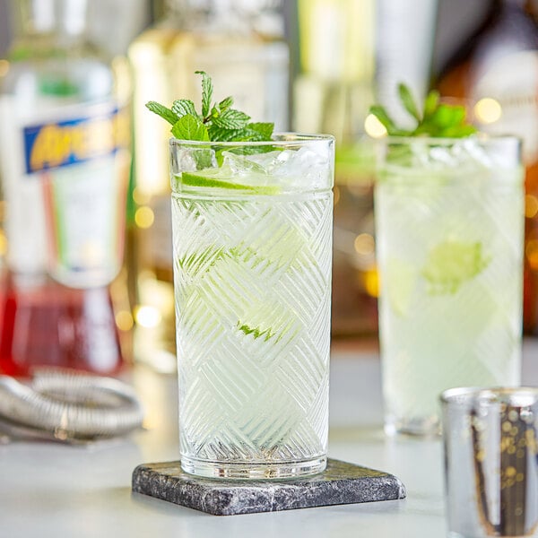 Two Acopa Zion beverage glasses filled with mint and lime juice on a bar counter.