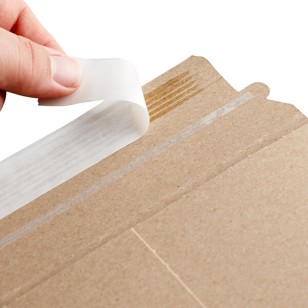 A person using a piece of tape to seal a Lavex Stayflats Kraft mailer box.