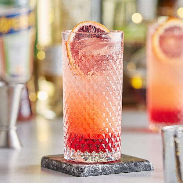 A highball glass of pink liquid with orange slices on top of it.