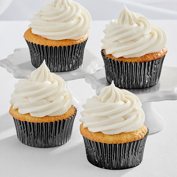 Three Enjay black foil baking cups with white frosting on cupcakes.