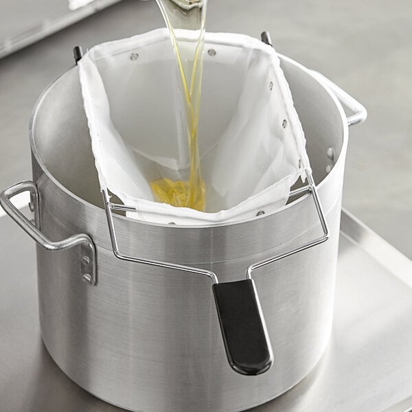 A person pouring oil from a bag into a metal pot on a counter.