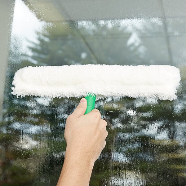 A hand using a green Unger StripWasher sleeve on a window.