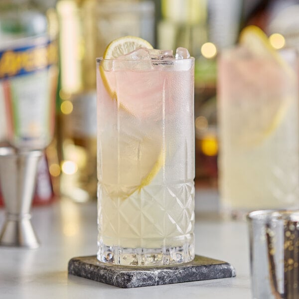 A glass of liquid with ice and a lemon slice in an Acopa Evora beverage glass.