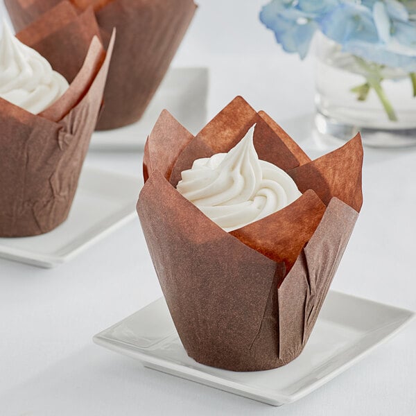 A close-up of a cupcake in a brown tulip baking cup on a white plate.