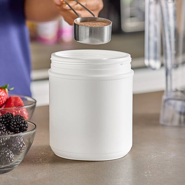 A person pouring brown powder into a 55 oz. white plastic canister.