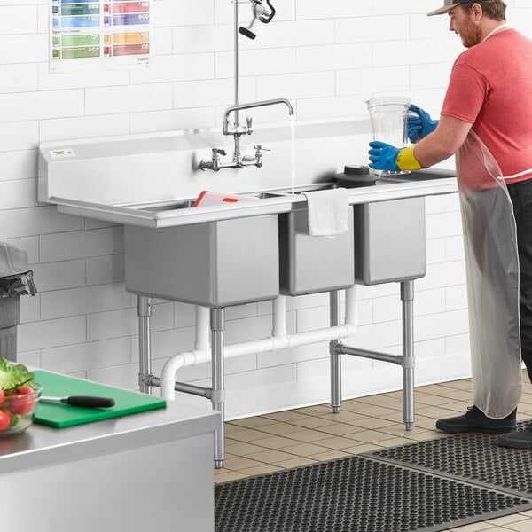 A man washing dishes in a Regency stainless steel three compartment sink with drainboards.