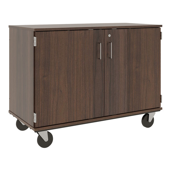 A dark brown wooden mobile cubbie storage cart with locking doors and wheels.